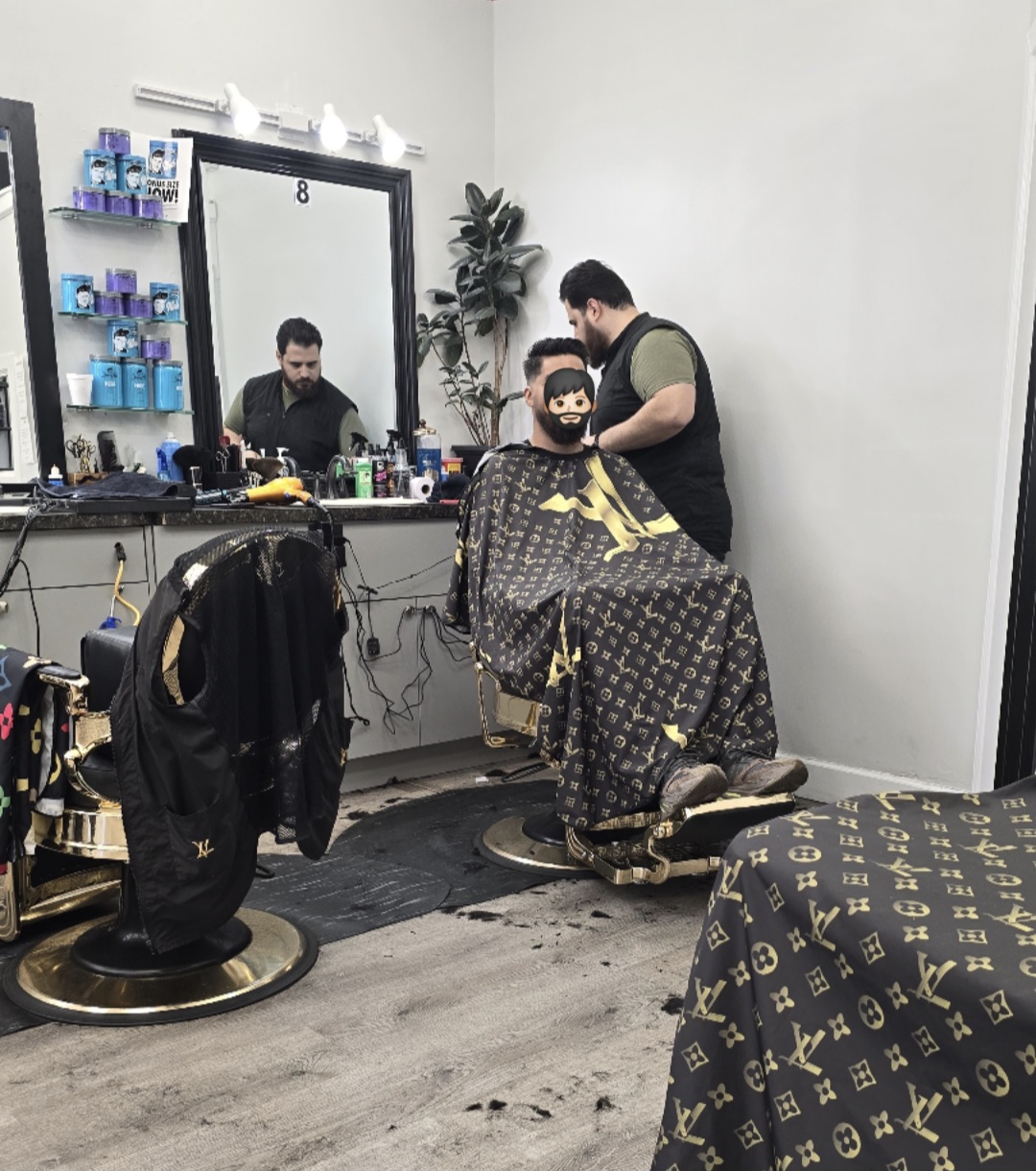A barber working at station 8 on a gold-based chair, with product stacked on glass shelves beside the mirror