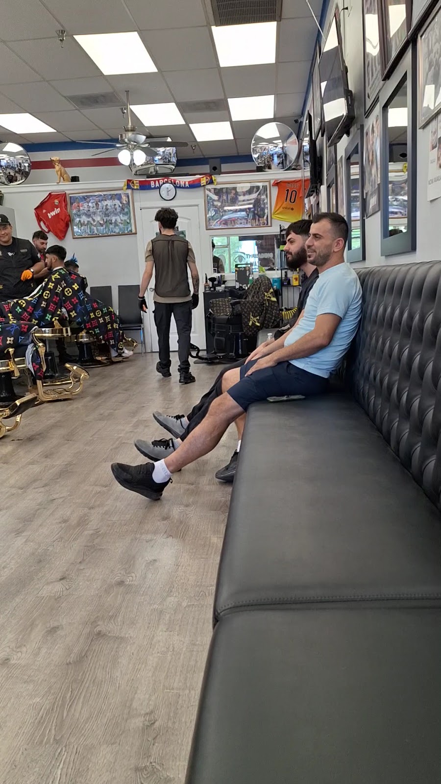 The long tufted waiting bench inside Spark Cutz, under a wall of framed photos, jerseys and a Barcelona scarf