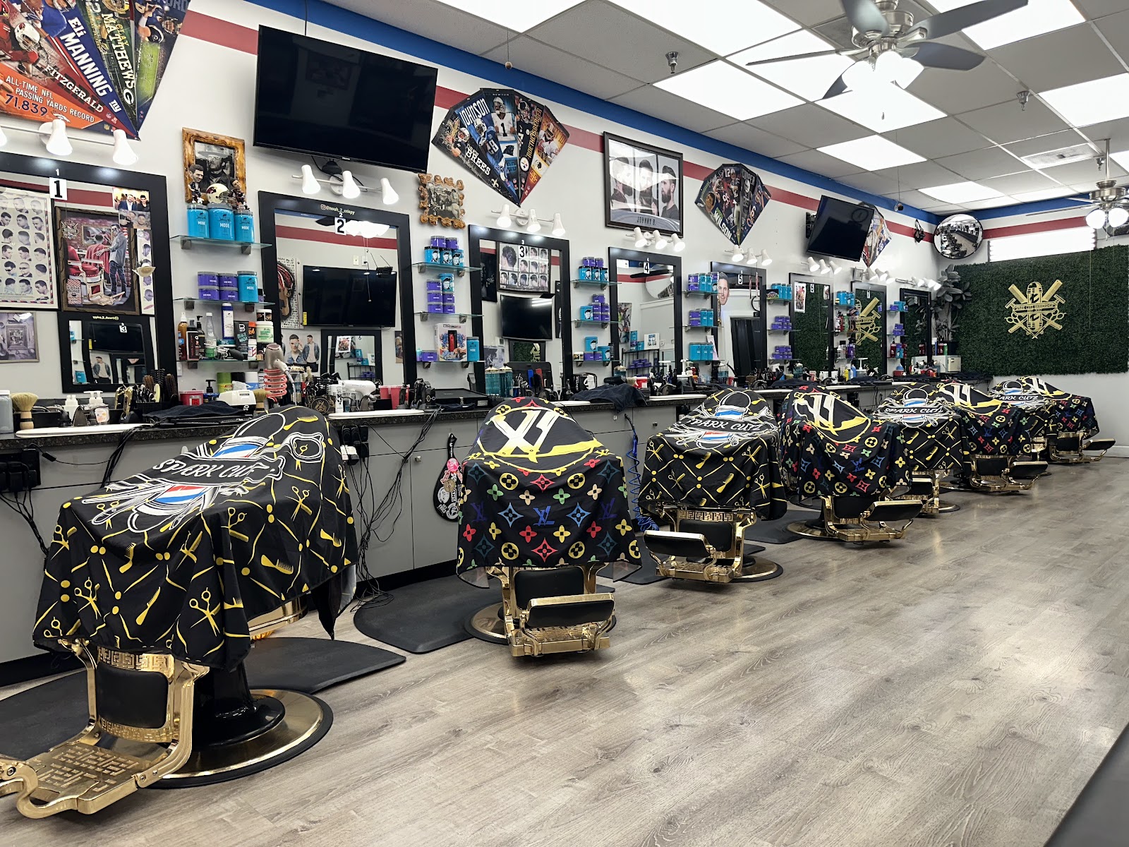 A row of eight ornate gold barber chairs at Spark Cutz, each draped in the shop's black capes printed with the sparkler logo and gold scissors